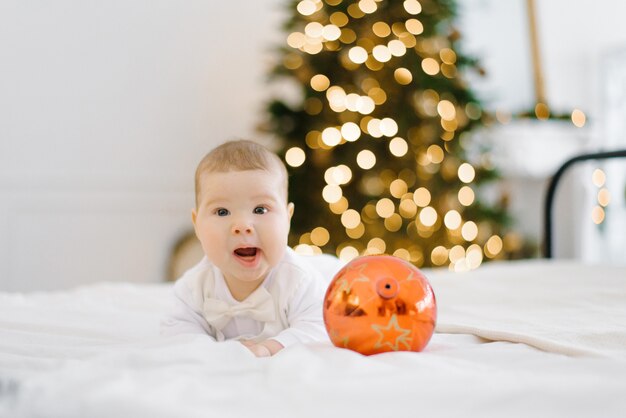 Baby laughs as he lies on the bed in the background of Christmas lights