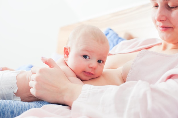 Baby laying on mothers belly bellow the breasts, looking at the camera. Mother is in comfortable and relaxed pose in laid-back breastfeeding position. Biological nurturing in supportive mothers arms.