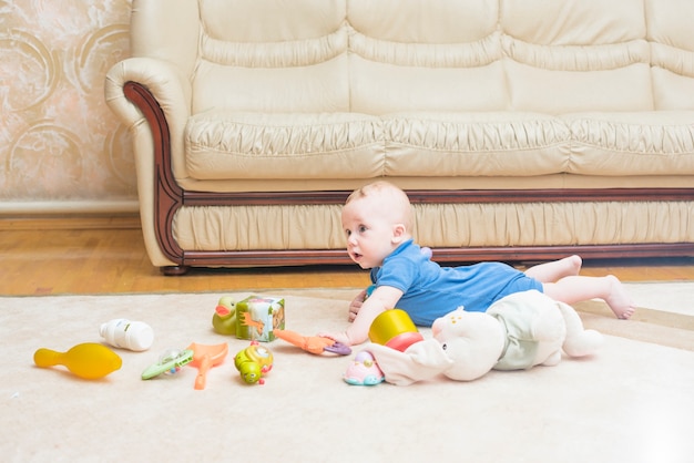 Baby laying with many toys on carpet at home