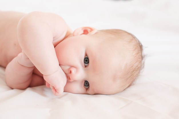 Baby lies on a bed on a white background with a hand in his mouth