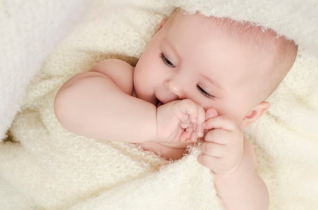 The baby lies on a light bed in a blanket smiling