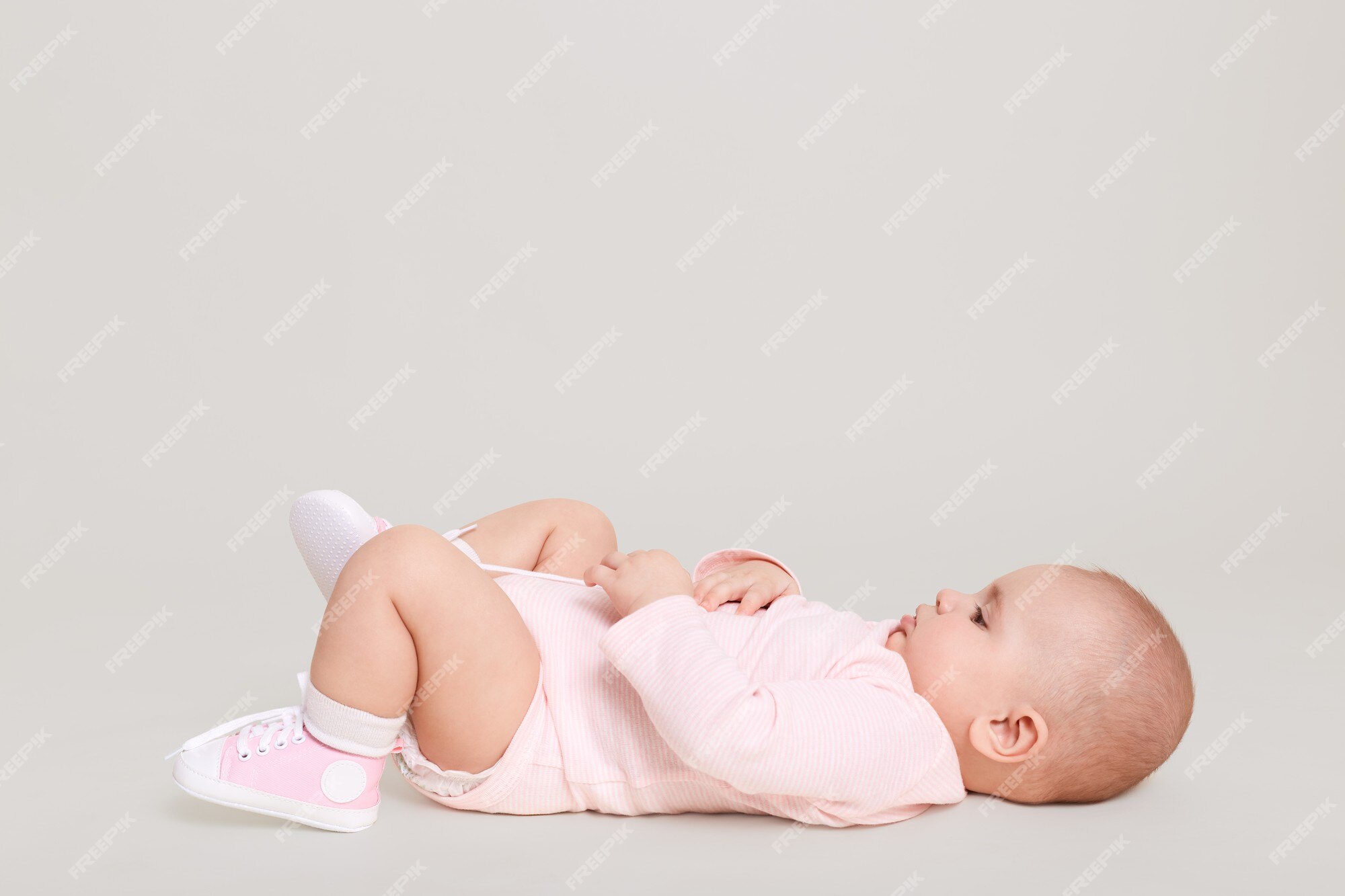 staan Baron Sentimenteel Baby liggend op de rug op de vloer terwijl poseren geïsoleerd over witte  muur. baby draagt een lichtroze bodysuit en kleine gympen, een klein kind  dat alleen binnen speelt. | Premium Foto