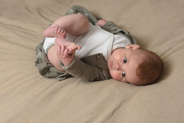 Baby liggend op het bed en houdt zijn voet met zijn handen vast