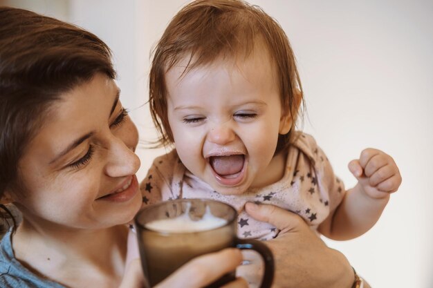 Baby little girl drinking a milk from cup while is holding by the moms arms happy people healthy meal