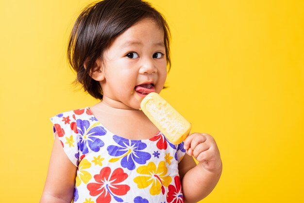 ディックパターンのシャツを着ている赤ちゃんの小さな女の子の笑顔は甘い木製アイスクリームを保持します