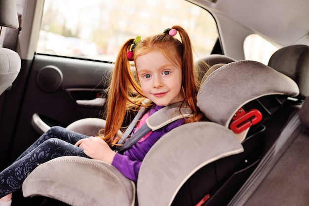 Photo baby little red-haired girl smiling while sitting in a child car seat.