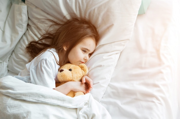 Baby lying in bed with taddy bear little girl sleeps with knitted toy