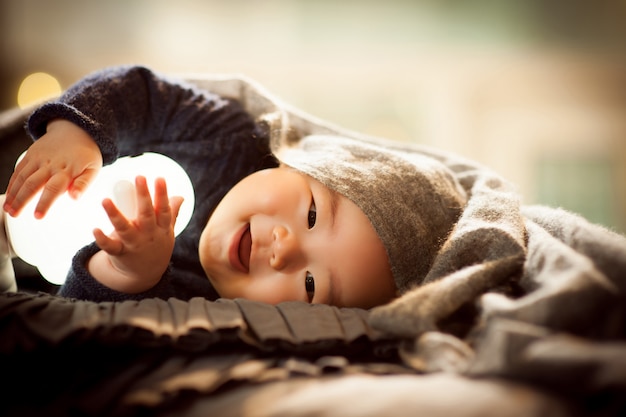 Un bambino sdraiato su un cuscino grigio si sta godendo la seduta della bambola e sorridendo brillantemente.