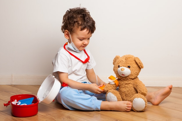 Baby in a medical mask plays with a teddy bear. Baby boy in a mask puts on a mask a toy.