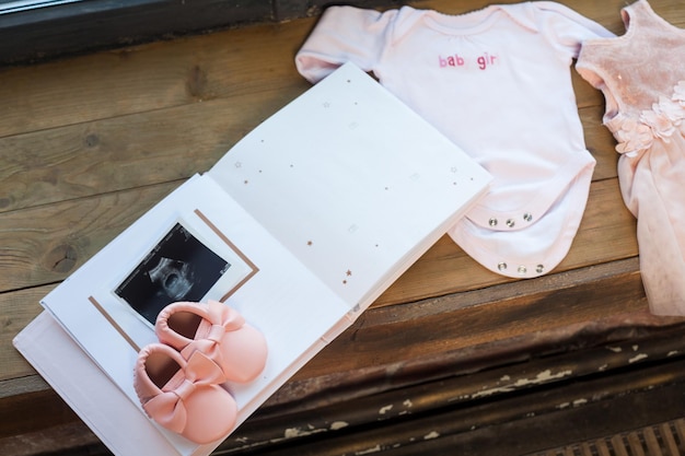 Baby meisje roze kleding met pasgeboren boek album, lichaam en kleine schoenen en echografie foetale foto op houten vensterbank achtergrond.