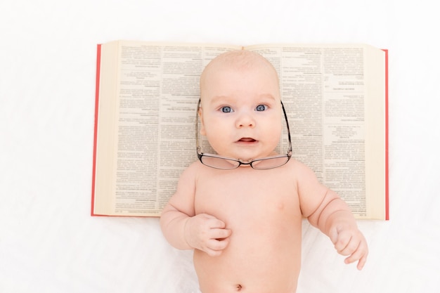 Foto baby met bril en een boek op een lichte achtergrond, leer- en ontwikkelingsconcept