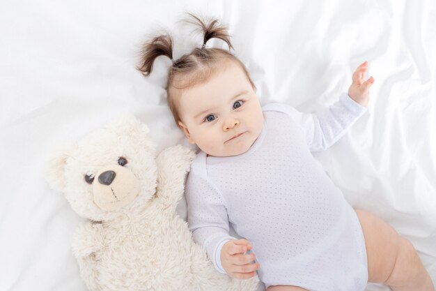 Baby met een teddybeer die thuis op het bed ligt, het concept van spelen en ontwikkeling van kinderen