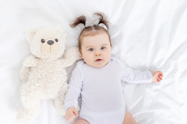 Baby met een teddybeer die thuis op het bed ligt, het concept van spelen en ontwikkeling van kinderen