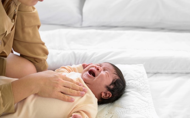 Baby newborn girl crying with mother comforting in bed at home