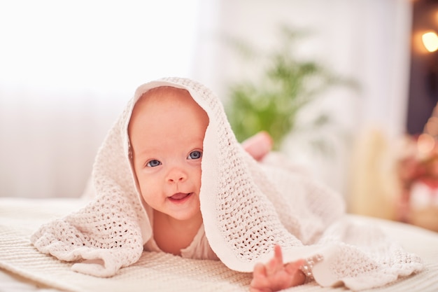 Baby onder de handdoek. een vrolijk klein kind kijkt onder de deken uit en lacht grappig. liggend op zijn buik op hun eigen hoofd.