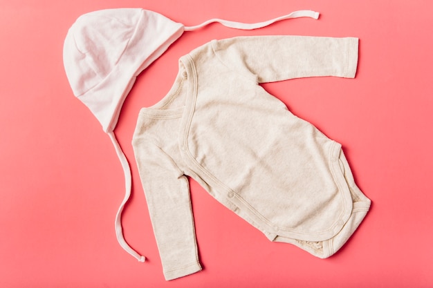 Baby onesie and headwear cap on bright background