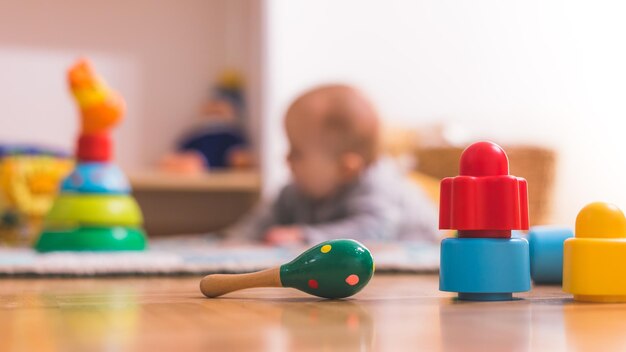 Baby peuter spelen concept Kleurrijke rammelaar en blokken op de voorgrond spelende baby in de onscherpe achtergrond