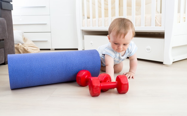 Baby playing on floor with fitness mat and dumbbells. Concept of child sports