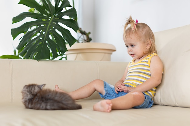 Baby playing with a little kitten on the couch