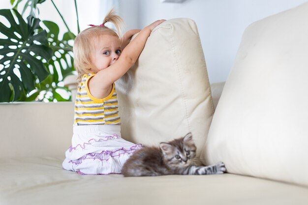 Baby playing with a little kitten on the couch