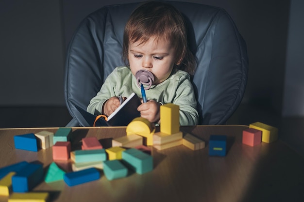 Bambino che gioca con un taccuino seduto davanti a un tavolo pieno di blocchi di costruzione sviluppo del bambino