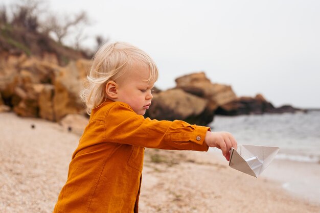 The baby playing with paper boat in the beach in autumn time