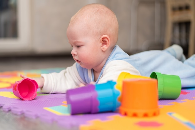 A baby plays on the floor. The child is lying on his stomach on rug with a pyramid.