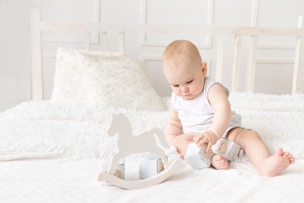 Baby plays with wooden toys cubes on the bed in a bright room