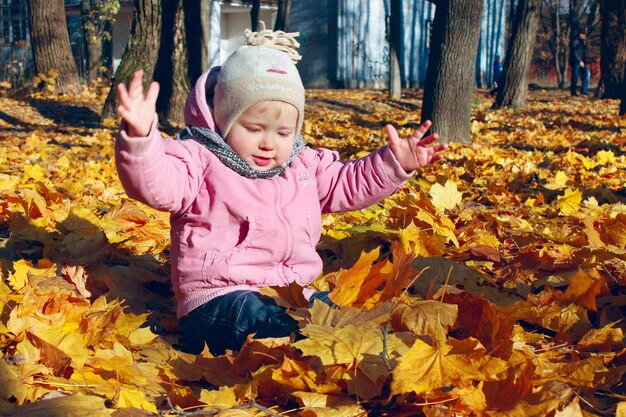 baby plays with yellow Autumn leaves in the park