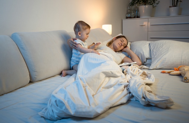 Baby probeert vermoeide moeder wakker te maken die in bed ligt te slapen