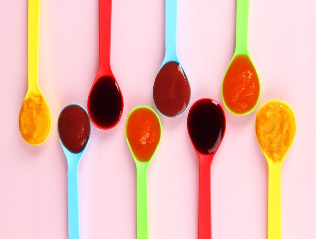 Baby puree in spoons on pink background