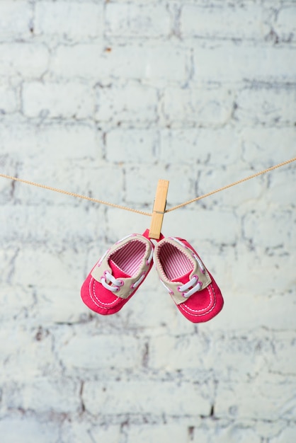 Scarpe rosse per bambini su una corda contro un muro di mattoni bianchi.