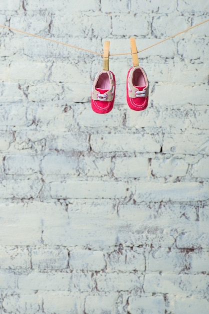 Baby red shoes on a rope against a white brick wall.