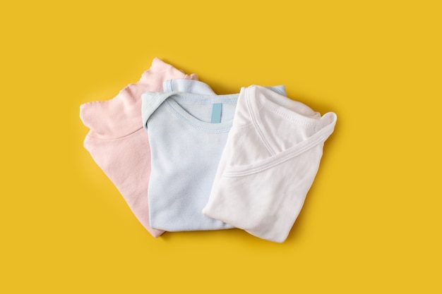 Baby romper of different colors on yellow surface