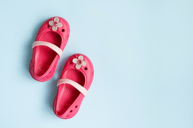 Baby roze rubberen zomer schoenen op blauwe muur met kopie ruimte