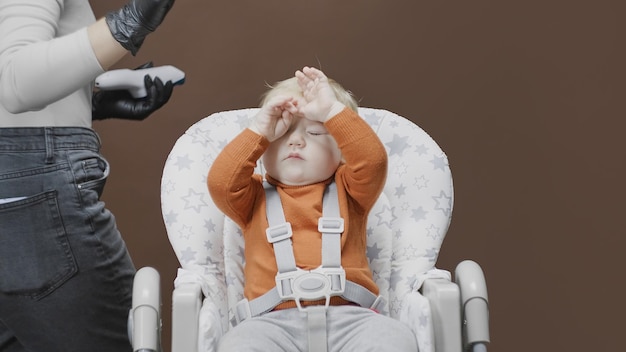 Baby rubs his eyes while sitting in feeding chair