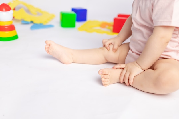 Baby's feet on a white isolated background among toys, space for text