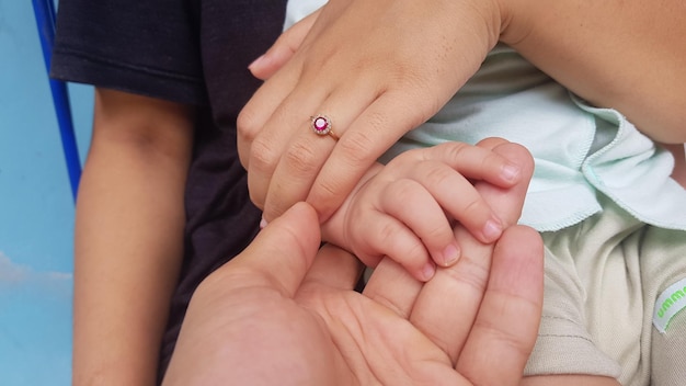 A baby's hand is held by a hand with a pink stone.