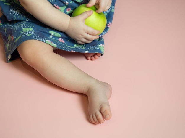 Baby's hands with a green apple on a pink background healthy food concept copy space