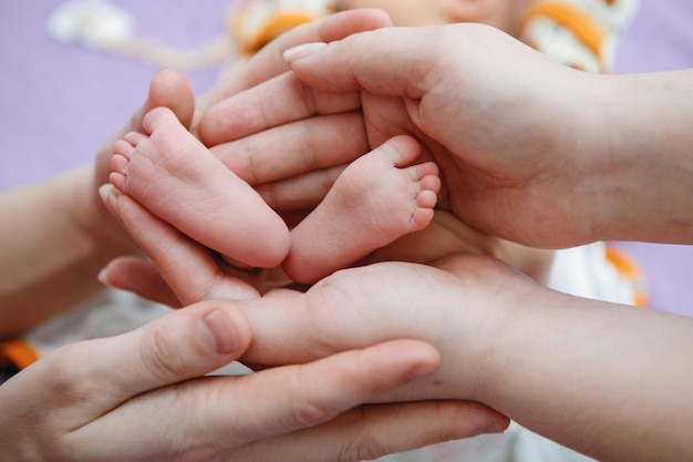 Foto le gambe del bambino nelle mani dei genitori. mamma e papà tengono i piedi di una figlia o di un figlio nei palmi delle mani. infanzia felice. cura dei genitori.