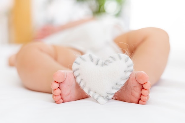 baby's small feet on a white bed with a plush heart a place for text closeup of a small child's feet and heart