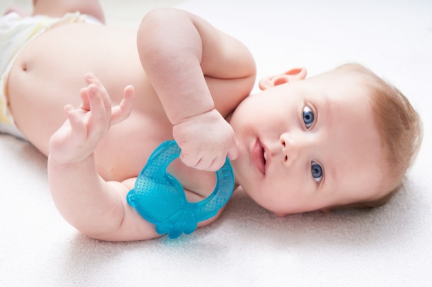 I denti del bambino vengono tagliati. ragazzo carino con occhi blu sgranocchia un giocattolo.