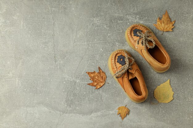 Baby shoes and leaves on gray textured background.