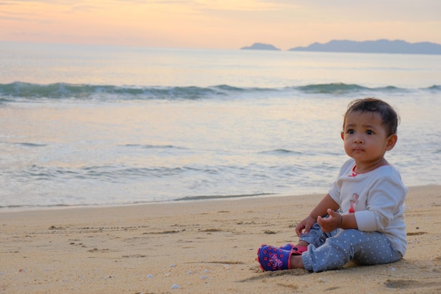 A baby sits on the beach at sunset