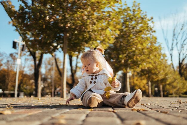 Photo a baby sits on a sidewalk in a park with a leaf in her hand.