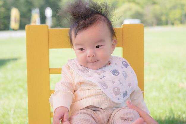 A baby sits in a yellow chair in a park.