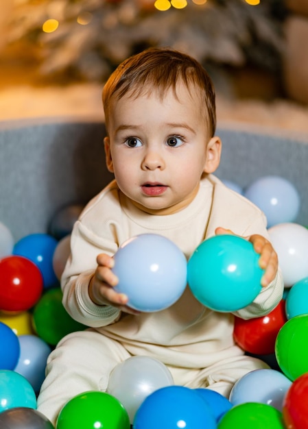 Photo a baby sitting in a ball pit surrounded by balloons baby having fun in a colorful ball pit