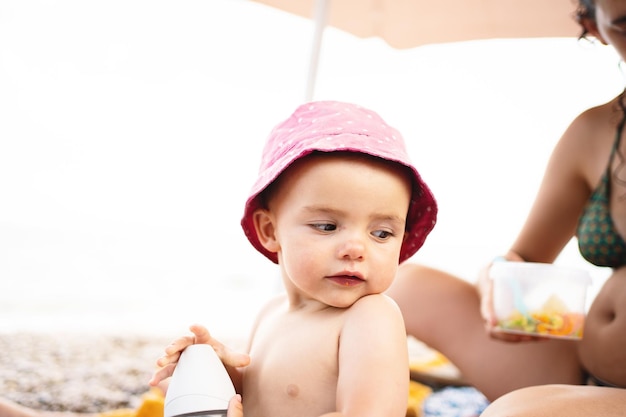 Bambino seduto sulla spiaggia accanto a sua madre sotto un ombrellone