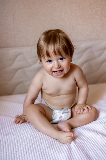 A baby sitting on a bed with a white and pink blanket.