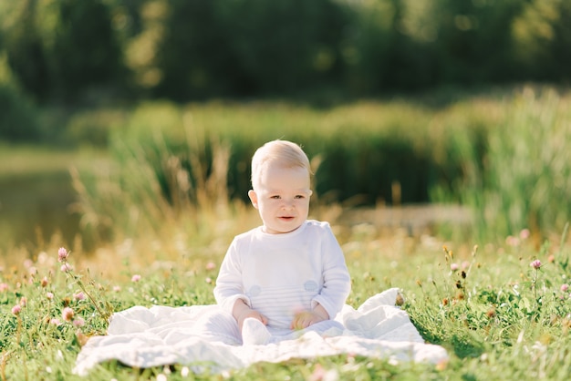 가벼운 bodysuit에서 자연에 격자 무늬에 앉아있는 아기